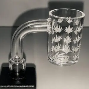 Grass Leave Glass Banger 14mm with little grass leafs on theres a shadow in the backgtround and its sitting on a black plinth